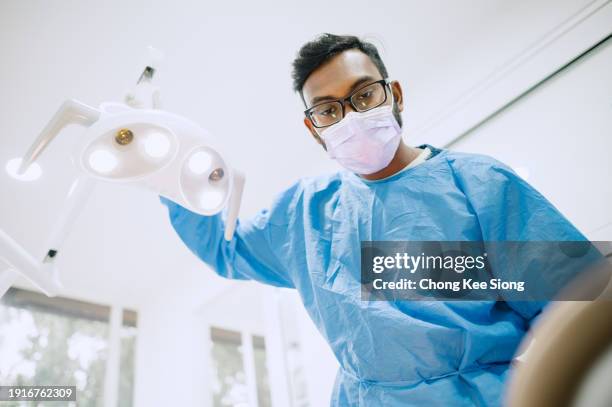 asiatischer indischer zahnarzt stellt das licht über dem zahnarztstuhl ein. - operationstisch stock-fotos und bilder
