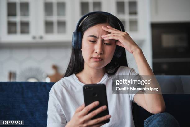 unhappy sad young asian woman with phone touching forehead, feeling upset and frustrated - lentezza foto e immagini stock