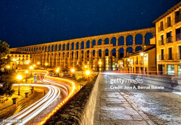 view of the city of segovia and the acueducto romano (roman aqueduct) to the light of the moon with the lights and trails of moving cars. - segovia stock pictures, royalty-free photos & images