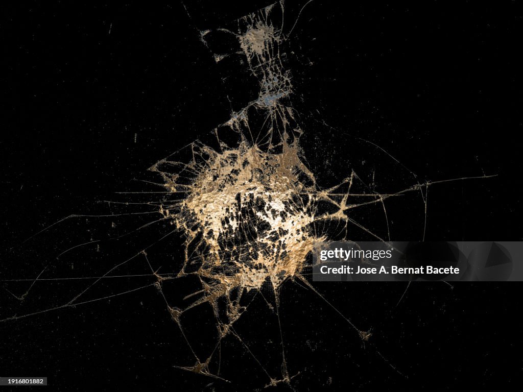Cracks and breaks in a glass surface from which golden metallic liquid comes out.