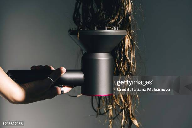 a woman dries wavy hair with a hair dryer with a special diffuser attachment. - secador de pelo fotografías e imágenes de stock
