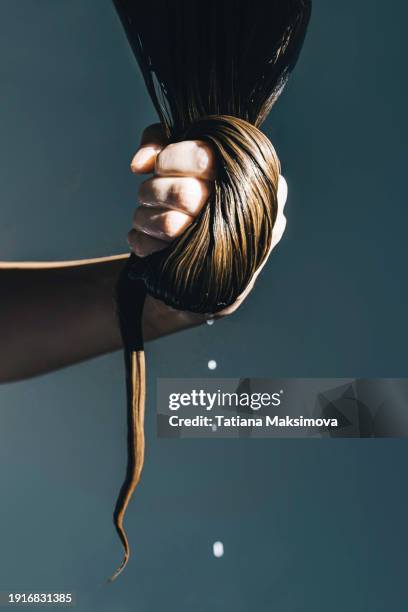 a woman's hand holds thick hair smeared with hair mask, drops dripping from the hair. - hair conditioner stockfoto's en -beelden