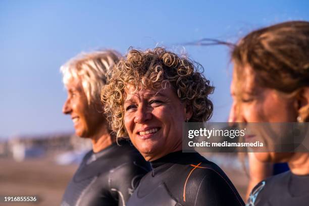 small group of middle-aged women friends sportswomen and open water swimmers prepare in a feel-good environment before entering the sea. - mature woman in water stock pictures, royalty-free photos & images