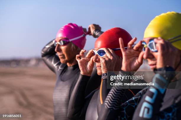 un pequeño grupo de amigas de mediana edad, deportistas y nadadoras de aguas abiertas se preparan en un ambiente agradable antes de entrar en el mar. - deporte acuático fotografías e imágenes de stock