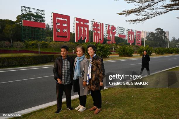 People pose in front of a giant propaganda slogan which reads "One Country, Two Systems, Unify China", which can be seen from Taiwan's Kinmen Island,...