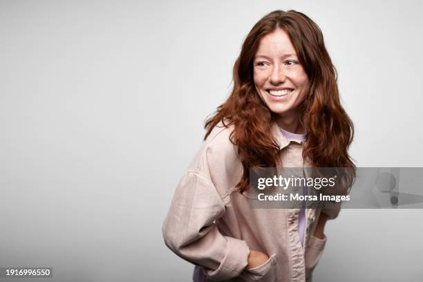 portrait of ginger young smiling woman looking over her shoulder against white background - retrato imagens e fotografias de stock