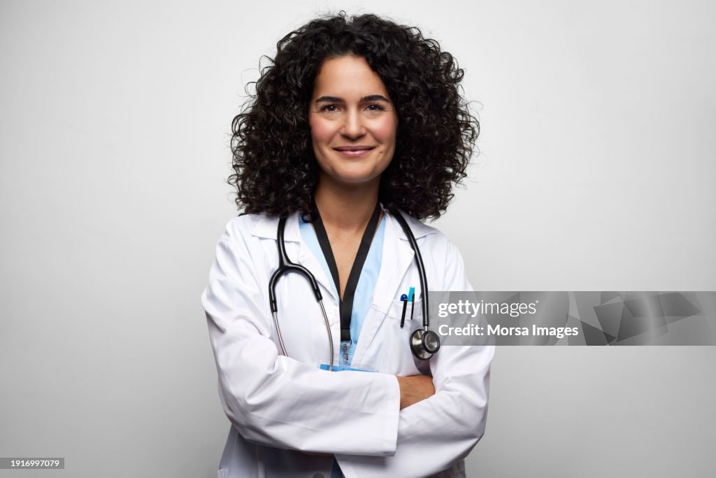 Confident Female Doctor With Arms Crossed Against White Background