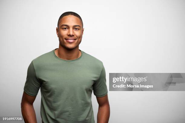 portrait of young man wearing green t-shirt. he is smiling against white background. - foto ritratto ufficiale foto e immagini stock