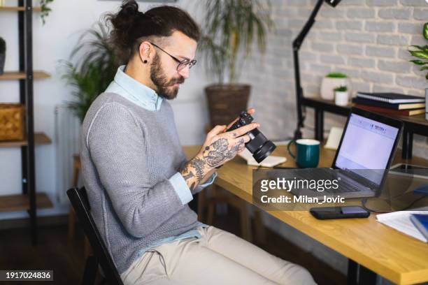 young man photographer looking at images on camera while working in studio - spiegelreflexkamera stock-fotos und bilder