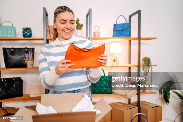 young woman starting small business selling homemade bags on line and packing them in cardboard box - box purse foto e immagini stock