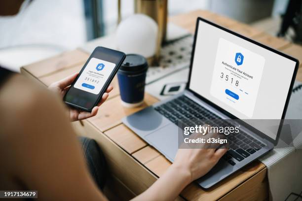 over the shoulder view of young woman using mobile device with two-factor authentication (2fa) security while logging in securely to her laptop. privacy protection, internet and mobile security - digitale authentifizierung stock-fotos und bilder