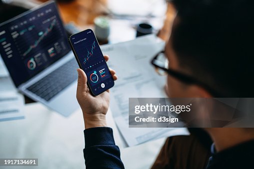 Young Asian man managing finance and investment online, analyzing stock market trades with smartphone and laptop. Making financial plans. Banking and finance, investment, financial trading, mobile banking with technology concept Young Asian man managing finance and investment online, analyzing stock market trades with smartphone and laptop. Making financial plans. Banking and finance, investment, financial trading, mobile banking with technology concept