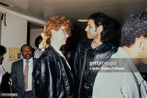 American actress Geena Davis, wearing a black leather jacket with her hair tied in a yellow bow, and her husband, American actor Jeff Goldblum, who...