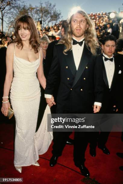 American actress Geena Davis, wearing a white evening gown, and her husband, Finnish film director Renny Harlin, who wears a black double-breasted...