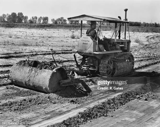 Man driving a Caterpillar D2 tractor fitted with a Killefer Tumblebug scraper, scraping earth from high places and placing it where drainage is poor,...