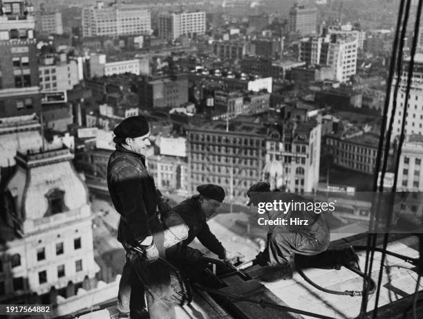 Group of construction workers, one man crouches to rivet girders of a construction frame, high up on a construction site with a view of the city...