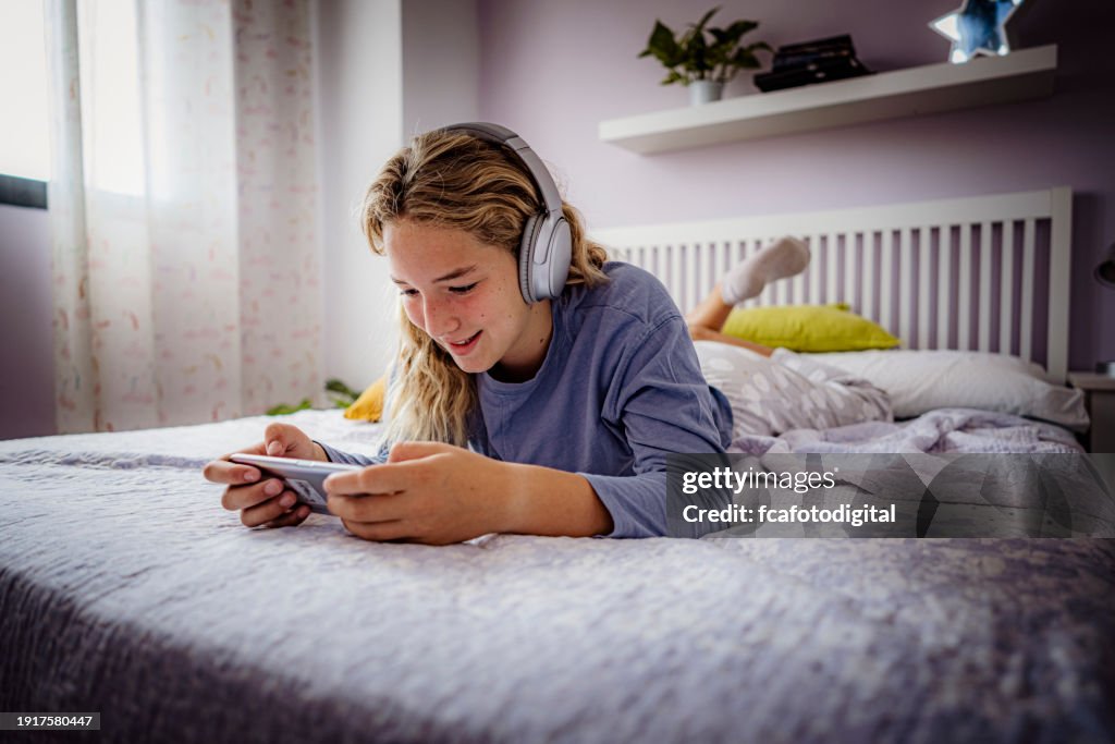 Teenager girl laying on bed using smartphone to play video games