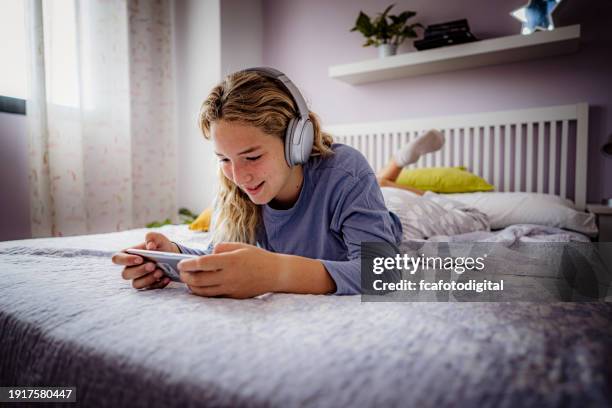 teenager girl laying on bed using smartphone to play video games - pre adolescent child stock pictures, royalty-free photos & images