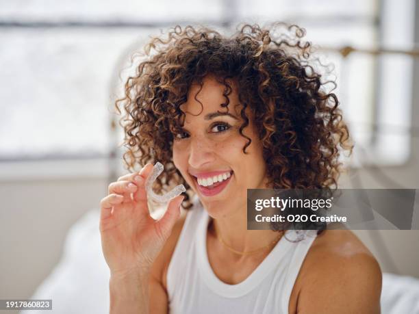 woman in bed in the morning using clear teeth aligners - aparelho dentário imagens e fotografias de stock