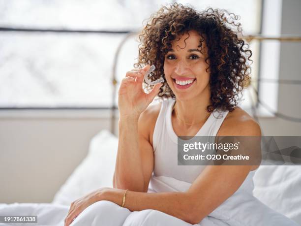 woman in bed in the morning using clear teeth aligners - aparelho dentário imagens e fotografias de stock