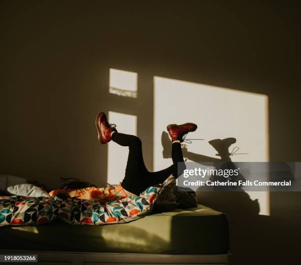 a child leaps onto a bed, casting a shadow on the blank wall beside her - sombra en primer plano fotografías e imágenes de stock