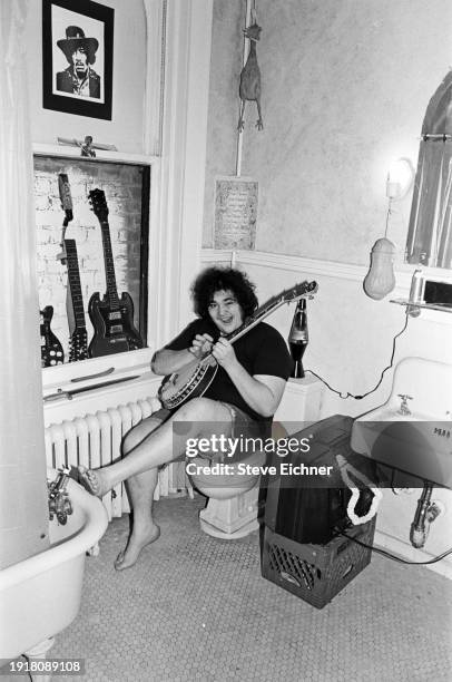 View of American Rock musician John Popper, of the band Blues Traveler, as he plays a banjo seated on a toilet in his Brooklyn home, New York, New...