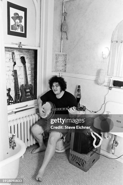 View of American Rock musician John Popper, of the band Blues Traveler, as he plays a banjo seated on a toilet in his Brooklyn home, New York, New...