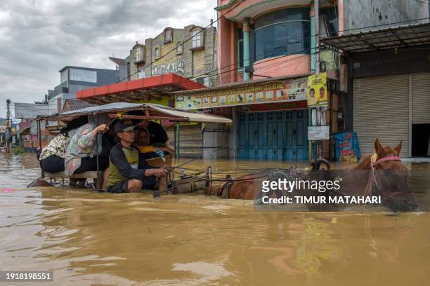 Residents evacuate using a horse-drawn carriage in the flooded town of Dayeuhkolot in Bandung on January 12 after a river overflowed due to heavy...