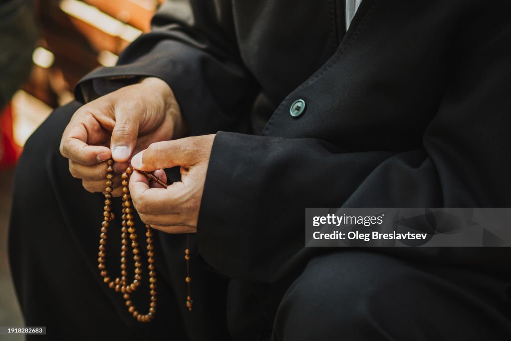 Prayer beads in male hands. Traditional religion black clothing.