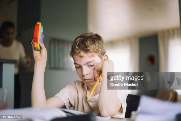 boy holding push pop toy and pencil while doing studies at home - autism spectrum stock pictures, royalty-free photos & images