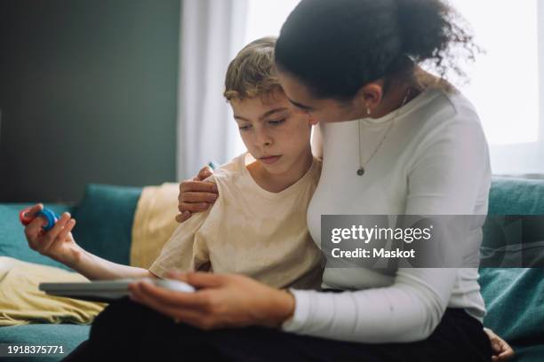 mother with arm around son sitting on sofa at home - autismo foto e immagini stock