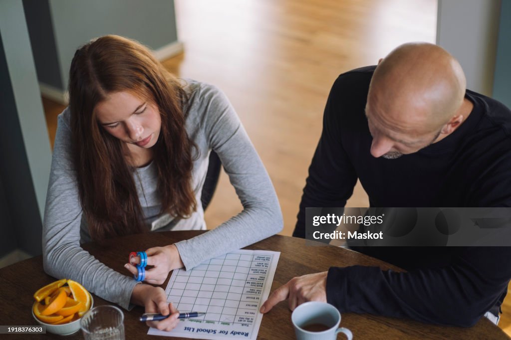 High angle view of father and daughter preparing school list while sitting at home
