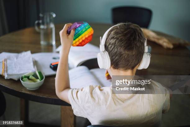 rear view of boy listening to music and playing with push pop toy while doing homework - neurodiversidad fotografías e imágenes de stock