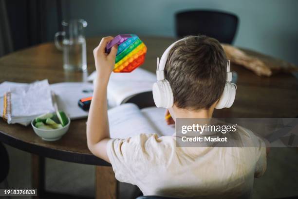 rear view of boy listening to music and playing with push pop toy while doing homework - adhd child imagens e fotografias de stock