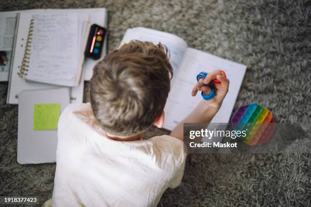 directly above view of boy fidgeting with ring toys while doing homework at home - autismo foto e immagini stock
