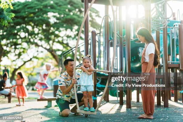 petite fille heureuse jouant sur l’aire de jeux avec ses parents - peuple eurasien photos et images de collection