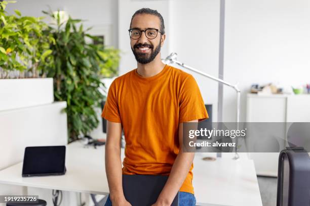 porträt eines glücklichen jungen mannes aus dem nahen osten, der an seinem schreibtisch im startup-büro sitzt - nordafrikanischer abstammung stock-fotos und bilder