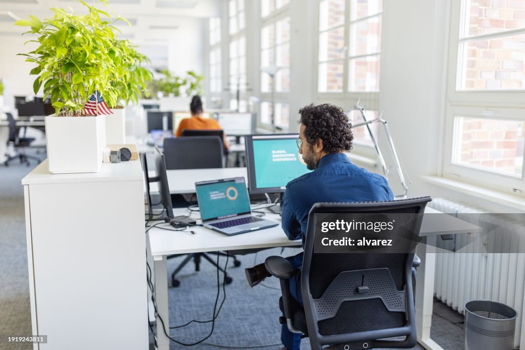 Young man busy working on laptop and desktop computer at office