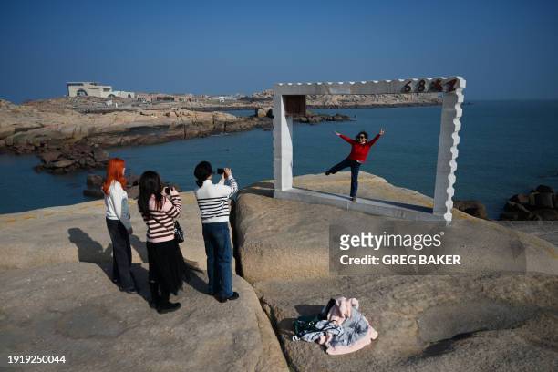 People take photos under a frame in front of the Taiwan Strait which marks the closest point in the mainland to the main island of Taiwan, on Pingtan...