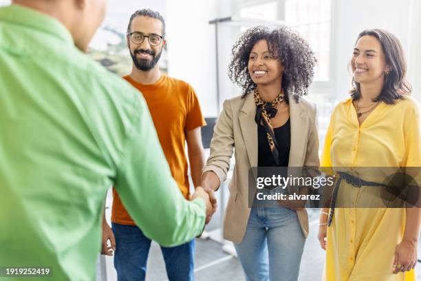 frau schüttelt dem mann die hand mit kollegen, die im büro bereitstehen - willkommen stock-fotos und bilder