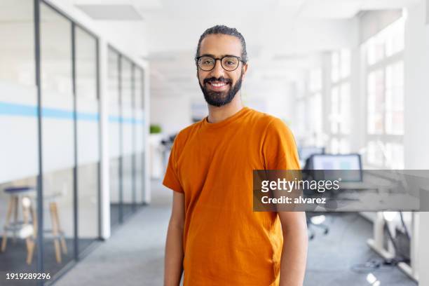porträt eines glücklichen jungen mannes, der im büro steht - nordafrikanischer abstammung stock-fotos und bilder