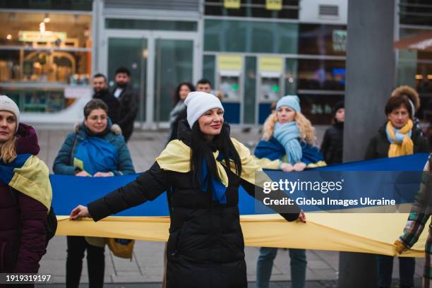 March participants stands with an unfurled 100-meter-long Ukrainian flag near the city's central railway station on January 6, 2024 in Cologne,...