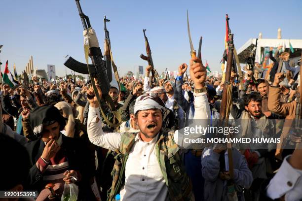 Huthi fighters brandish their weapons during a protest following US and British forces strikes, in the Huthi-controlled capital Sanaa on January 12,...
