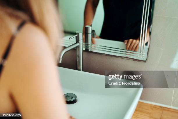 a woman washing her hands in the sink under the faucet - brechreiz stock-fotos und bilder