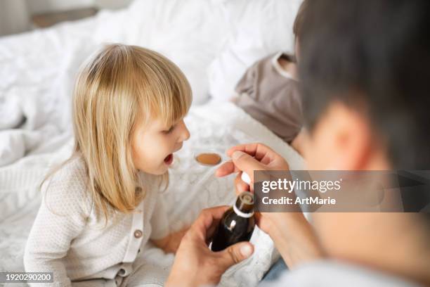 father giving syrup to his sick little girl with flu, cold, coronavirus, bronchitis or pneumonia, virus or infection - taste for a cure stock pictures, royalty-free photos & images