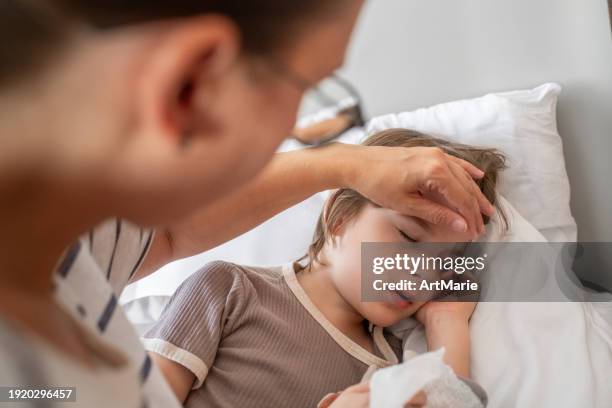 krankes kind, das mit grippe, erkältung, coronavirus, bronchitis oder lungenentzündung, virus oder infektion zu hause im bett schläft und seine mutter seine stirn berührt und die temperatur misst - sinusitis stock-fotos und bilder