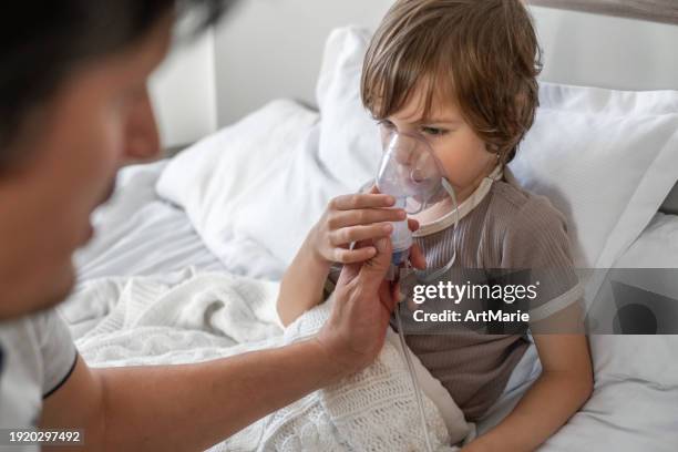 niño enfermo con padre hace inhalación con nebulizador en casa en la cama con asma, gripe, resfriado, covid, bronquitis o neumonía, virus o infección - neumonía fotografías e imágenes de stock