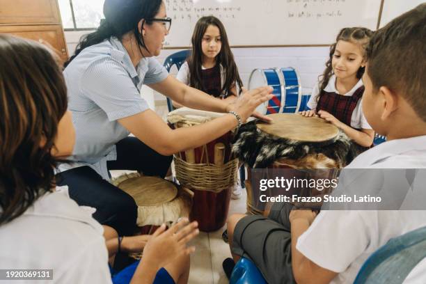 mature teacher teaching child students to play drum in school classroom - slaginstrument stockfoto's en -beelden