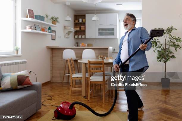 bearded mature man dancing happily with a vacuum cleaner - house cleaning stock pictures, royalty-free photos & images