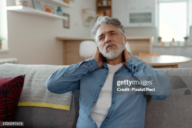 reifer erwachsener mann, der zu hause unter nackenschmerzen leidet - hals stock-fotos und bilder